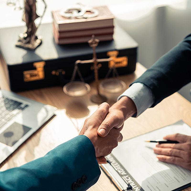 Two professionals shaking hands over a desk in an office.